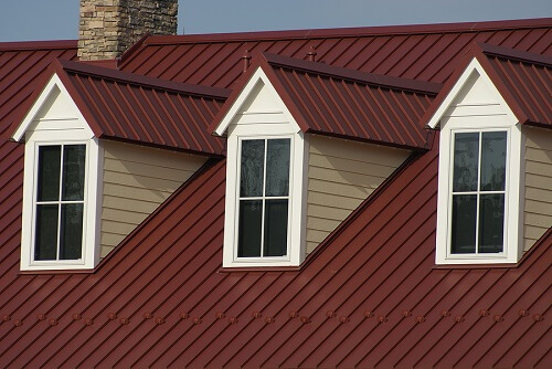 Which Metal Roof is Best? Standing Seam vs. Screw Down Panel | Pride Roofing LLC. Image of attic windows and red metal roofing.