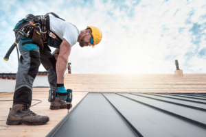 2024 Metal Roofing Cost in Hammond, LA. A roofer in safety gear installing metal panels on a roof under a bright sky, capturing the precision and effort involved in metal roofing installation.