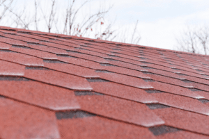 spring roof inspection, roofing and construction expert in Hammond, LA at Pride Roofing LLC. Image showing a close-up view of red asphalt shingles on a pitched roof.